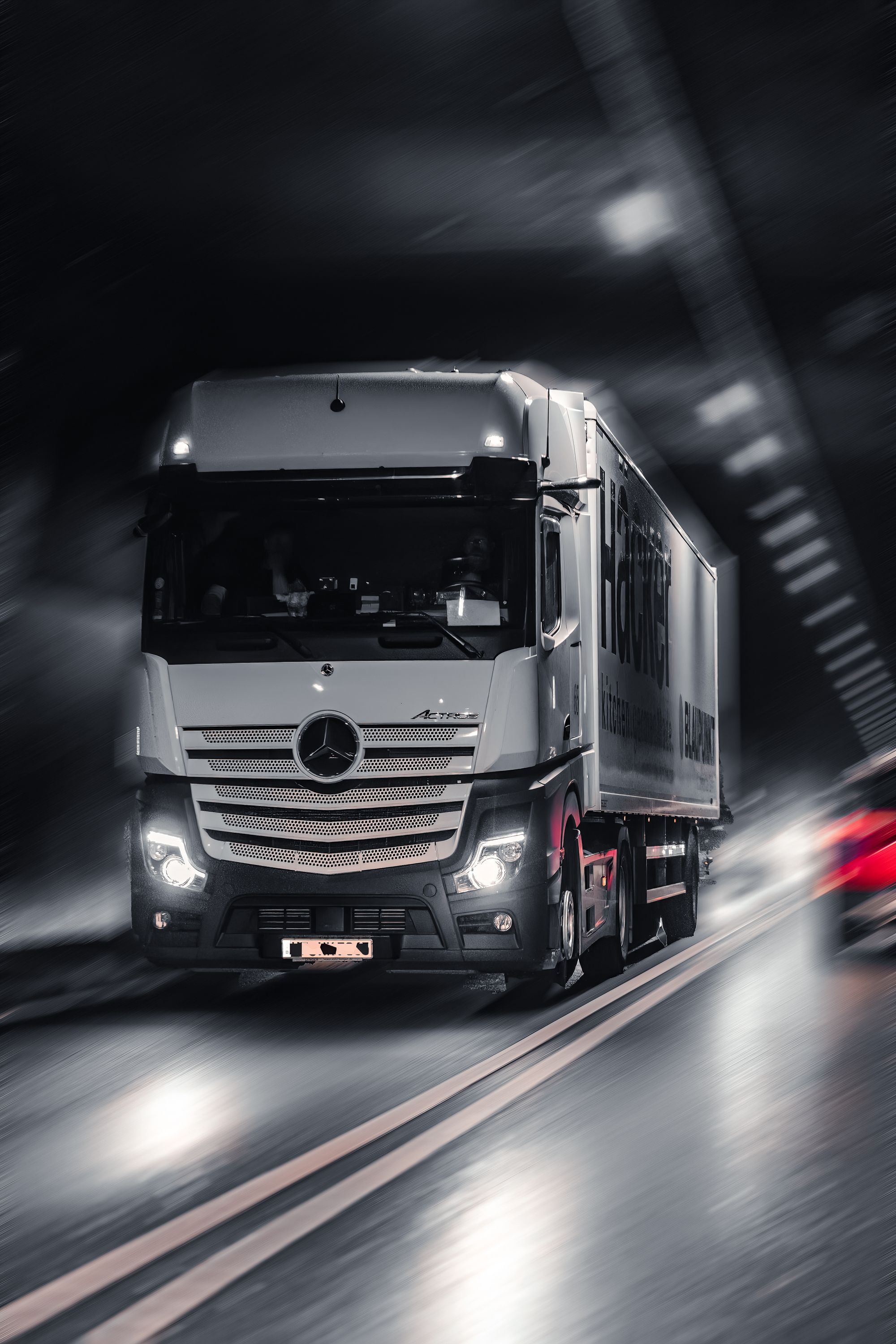 Schwerer LKW mit eingeschalteten Scheinwerfern in dramatischem Dämmerlicht auf der Fernstraße